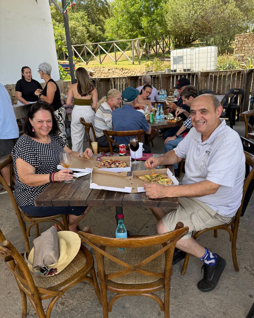 Guests smiling over boxed wood-fired pizzas at an outdoor lunch