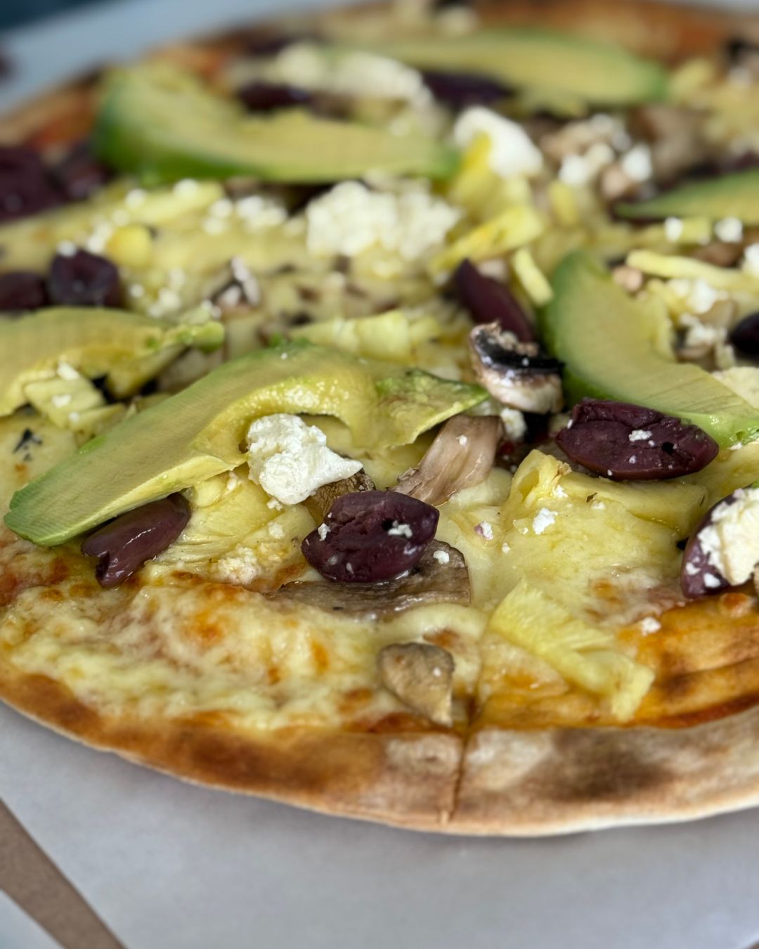 Close-up of a wood-fired pizza with avocado, feta, olives and mushrooms