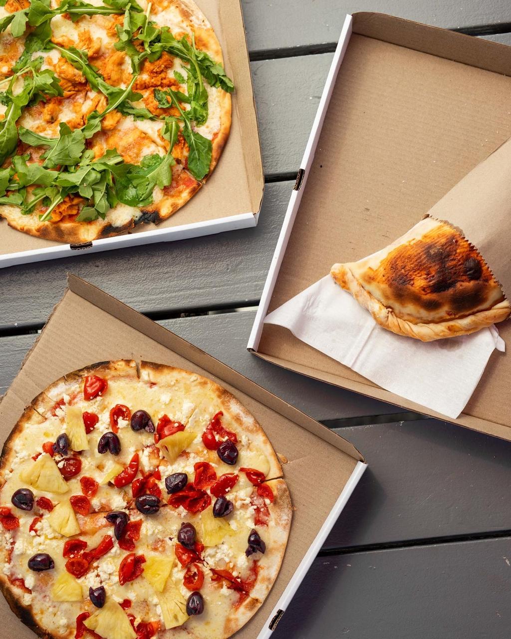 Two open pizza boxes and a folded calzone on a grey deck table