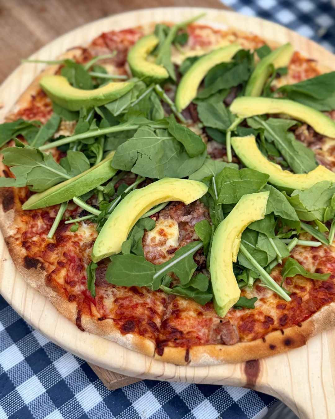 Bacon, avocado and rocket wood-fired pizza on a wooden board