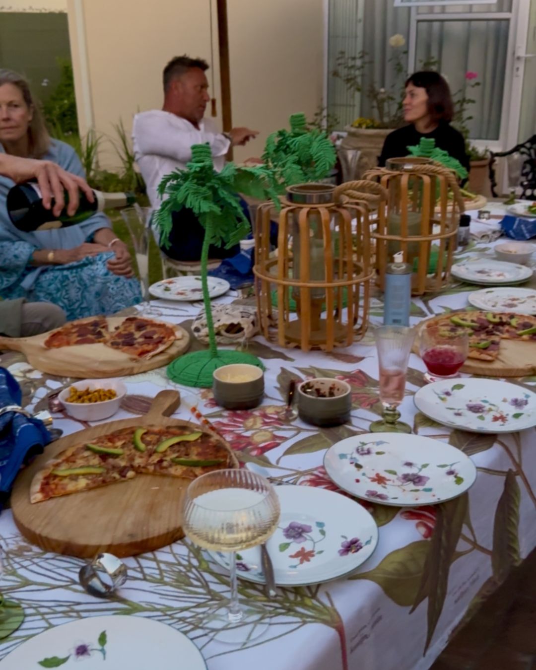A long table of guests, wine and wood-fired pizzas in a garden