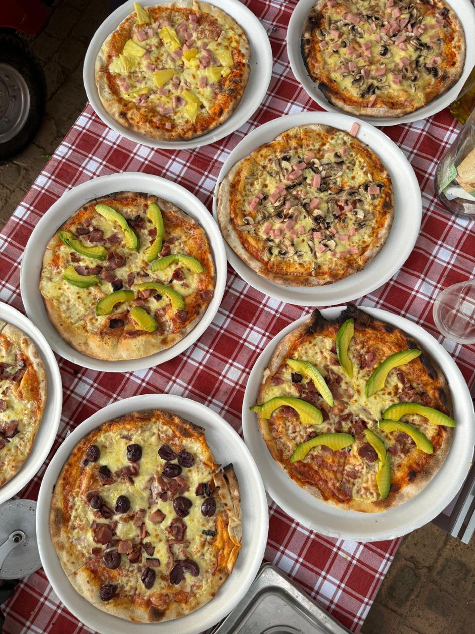 Seven wood-fired pizzas plated on a red checked tablecloth