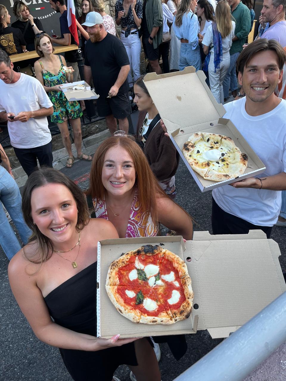 Guests holding open boxes of margherita and burrata pizza at a busy street event
