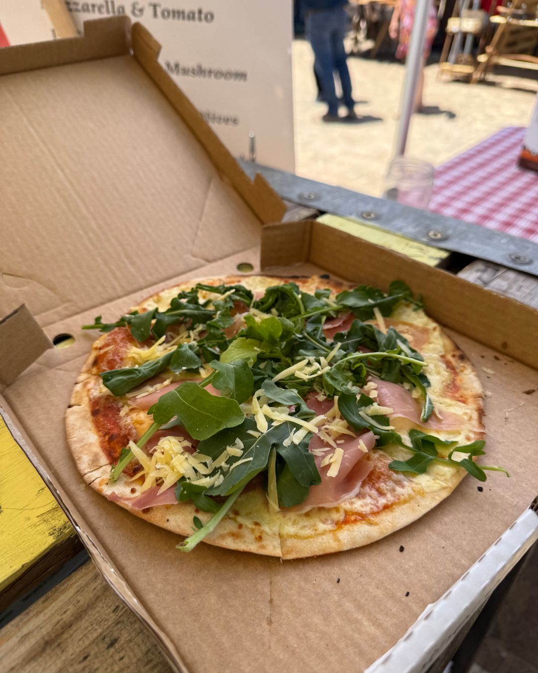 Prosciutto and rocket pizza in its box at an outdoor market setup