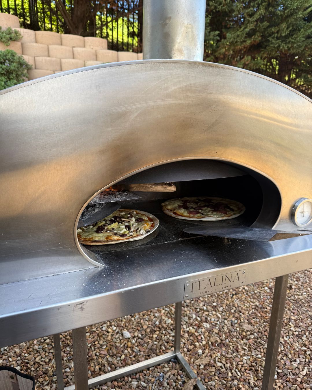 Two pizzas cooking on the stone floor of the Italina wood-fired oven